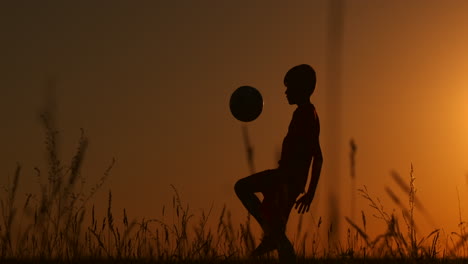 A-young-young-boy-football-player-trains-playing-with-a-ball-stuffing-on-his-leg-at-sunset-in-slow-motion-during-the-Golden-hour-in-the-field-until-sunset.-Training-from-dusk-to-dawn.-Concept-path-to-success