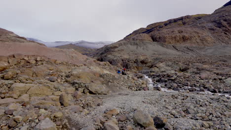 Hikers-Traveling-Towards-The-Bridge-Over-The-Rocky-River-in-Iceland