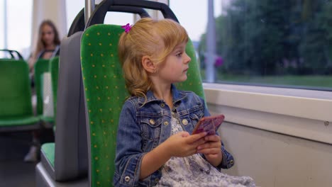 Little-girl-on-smartphone,-chatting,-texting,-browsing-social-media-while-traveling-by-bus-in-city