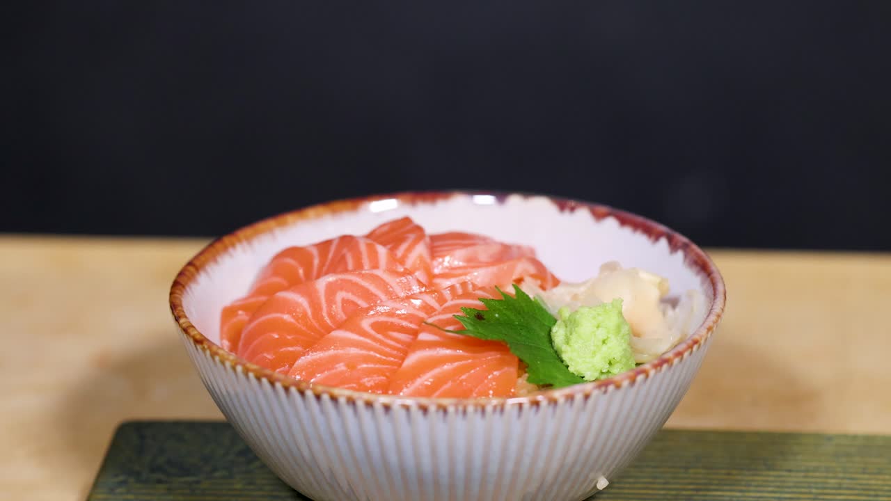 Un primo piano statico di una tradizionale ciotola giapponese di donburi di salmone su un tavolo di legno