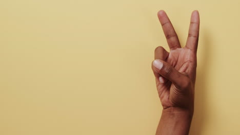 cerca de la mano de un hombre biracial mostrando un signo de paz con espacio de copia en fondo amarillo.