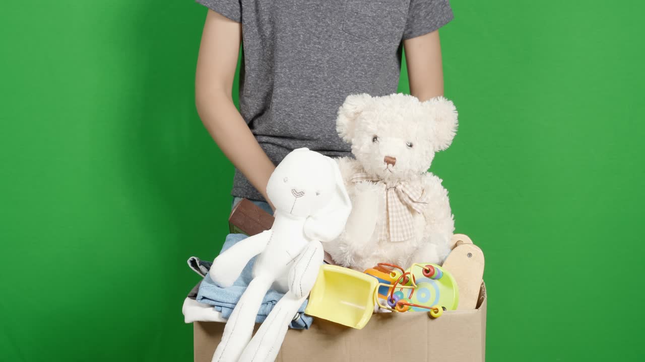 자선 기부를 위해 옷과 장난감을 준비하는 소년. 어린이 장난감을 분류하고 포장하는 소년, 어린이 옷을 녹색 화면 위의 카드보드 상자에 넣는 크로마 키 배경