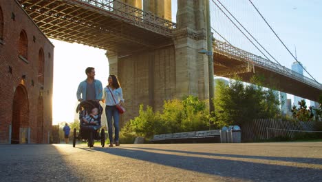 una joven familia con un cochecito caminando bajo un puente en manhattan