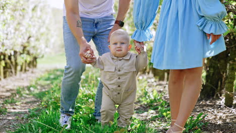 young parents of a cute toddler learning to walk outdoors. beautiful caucasian family portrait in the spring garden.