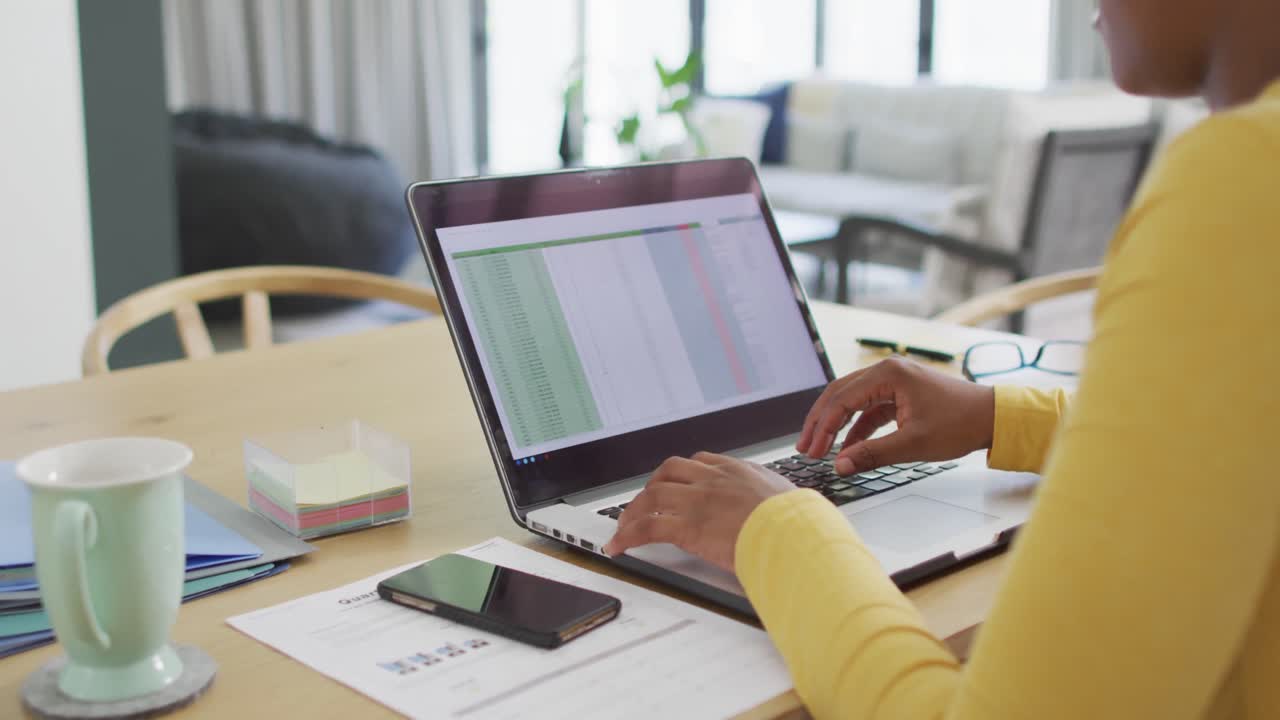 Happy african american woman sitting at table using laptop