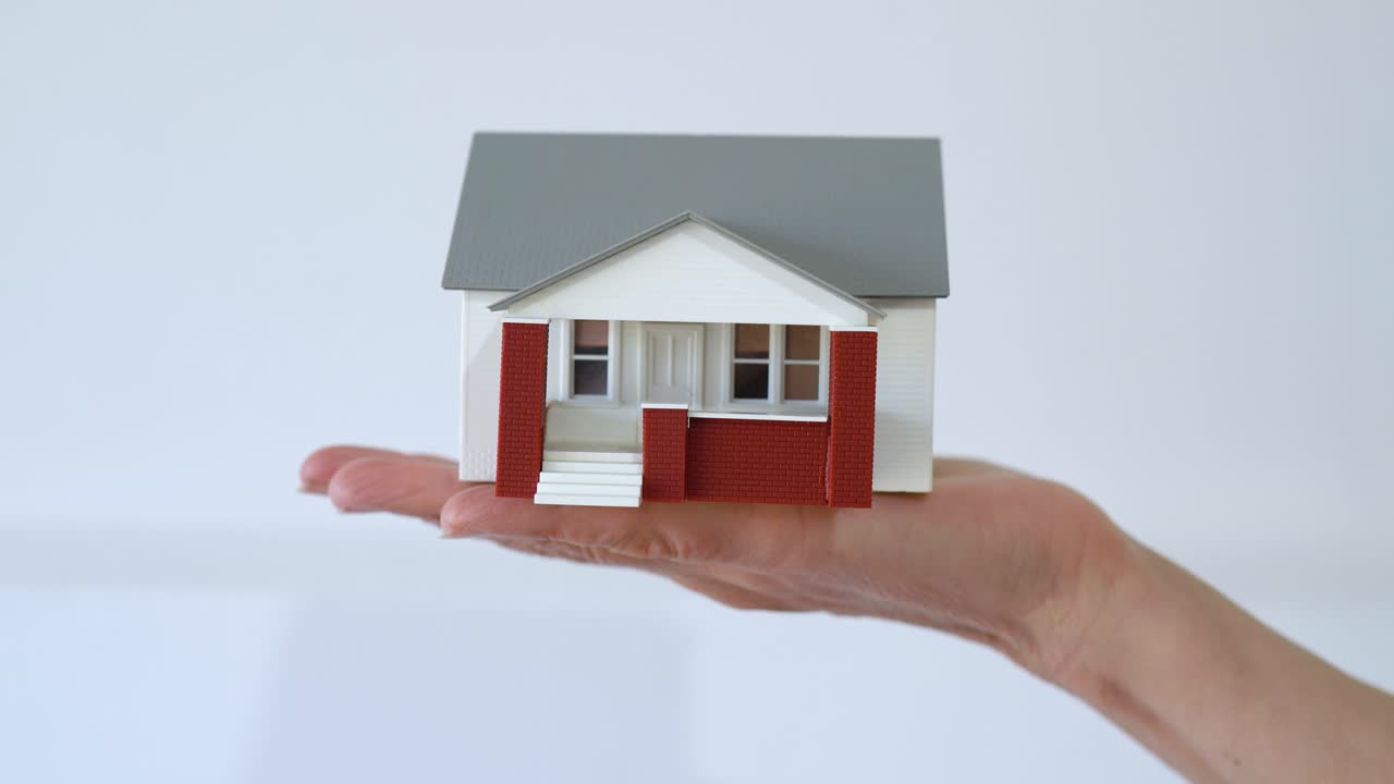 Hand Holds Miniature House Model On Its Palm Against Plain Background. Real Estate Concept. closeup shot