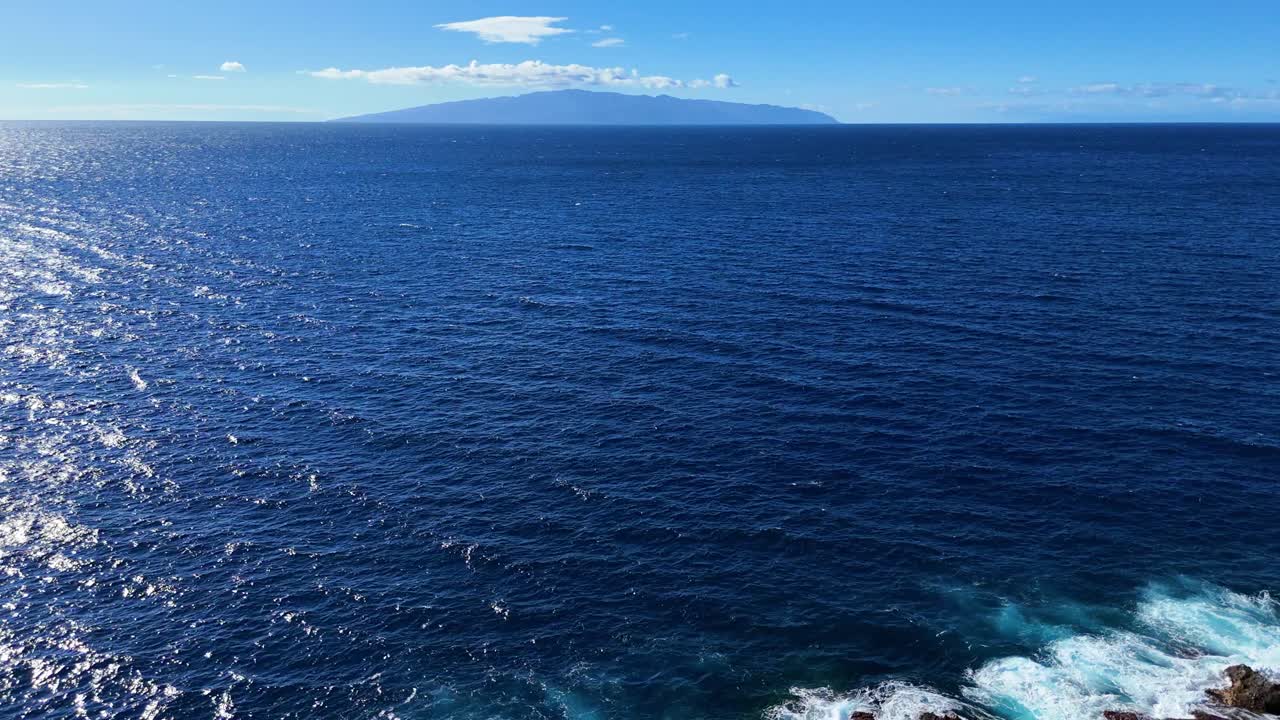 experimente las impresionantes vistas aéreas de la escarpada costa de tenerife, mostrando las vibrantes aguas azules y la encantadora isla de la gomera en un día despejado y soleado en las islas canarias.