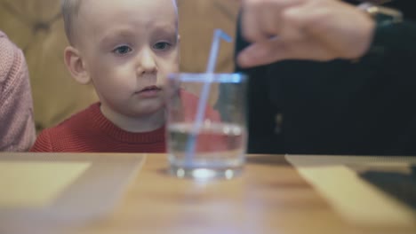 man in black makes bubbles in water with straw for happy son