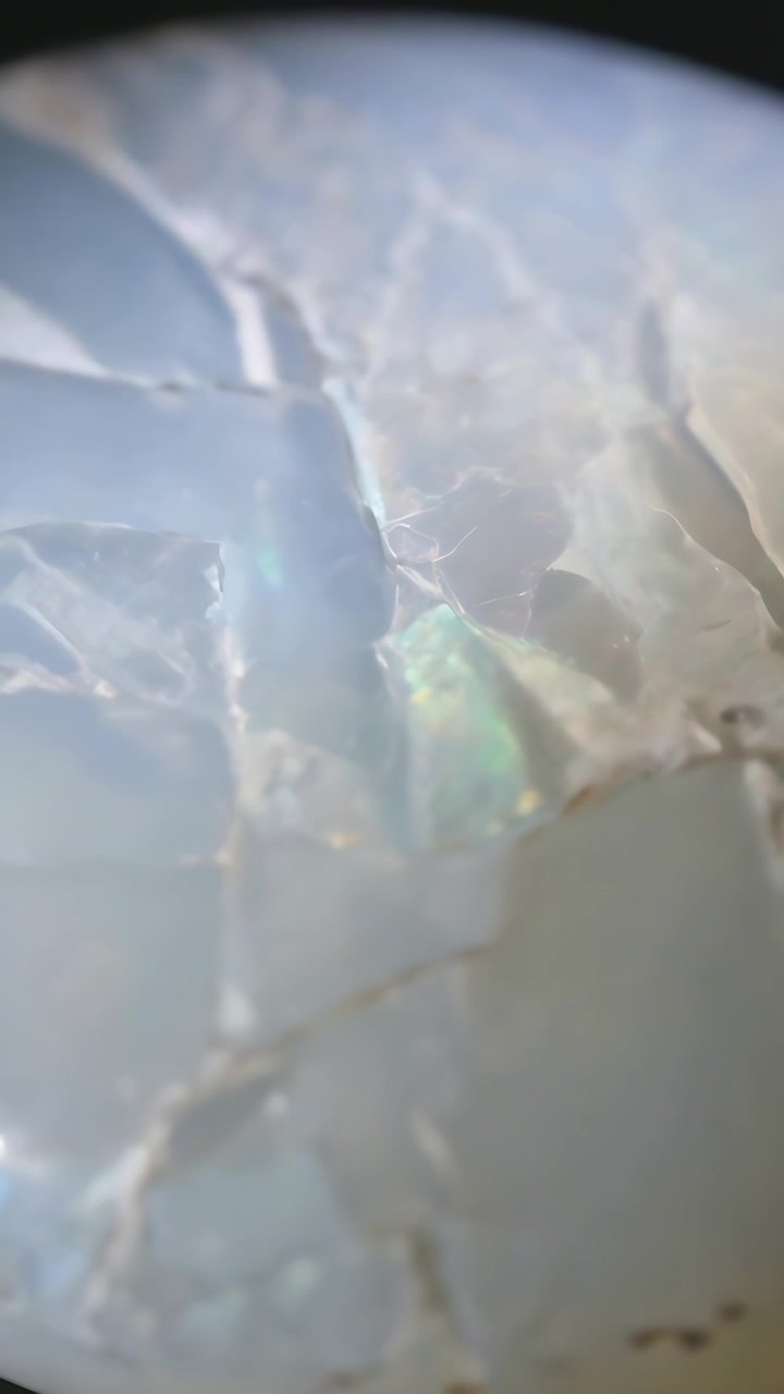 Vertical video: Shifting lighting and angle, opal displaying blue flash under loupe for inspection
