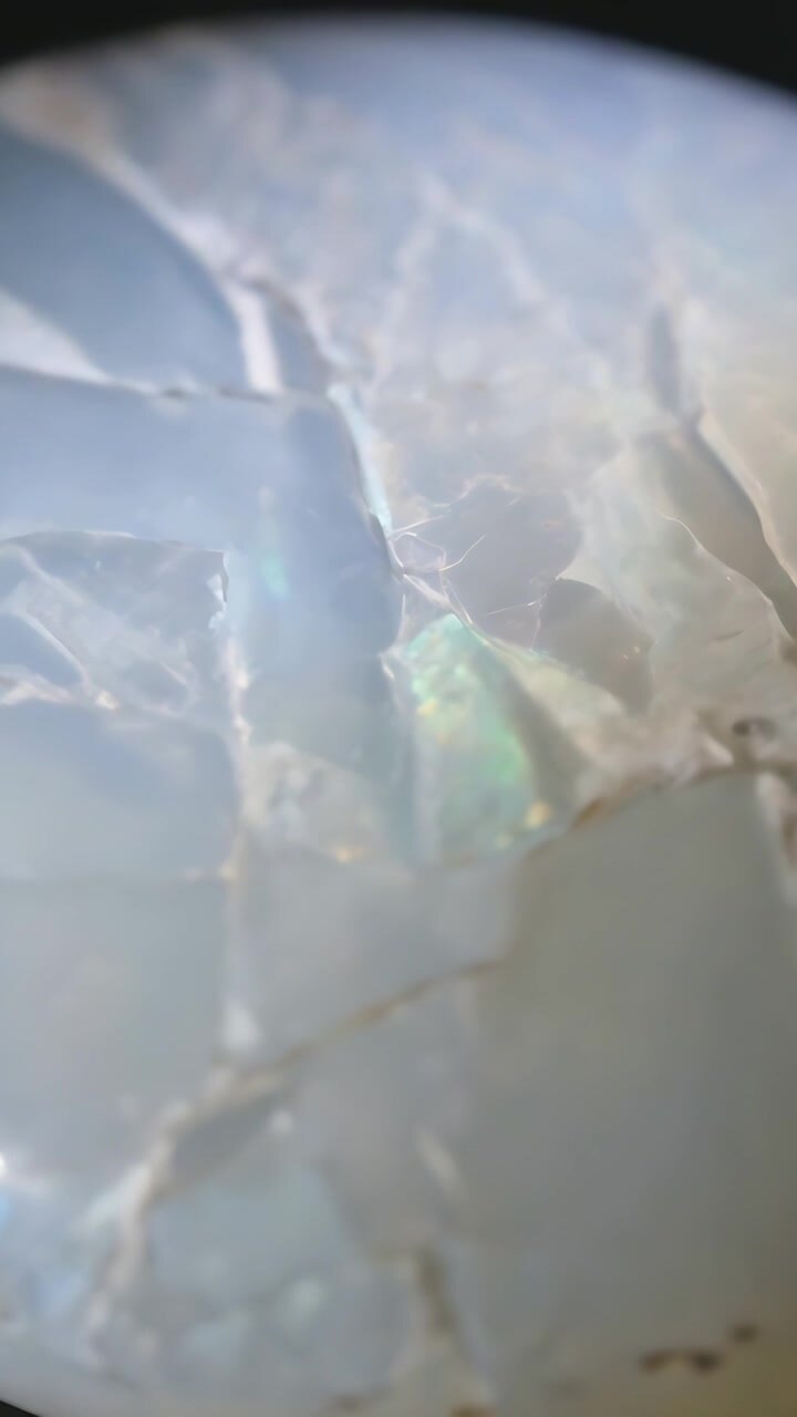 Vertical video: Shifting lighting and angle, opal displaying blue flash under loupe for inspection