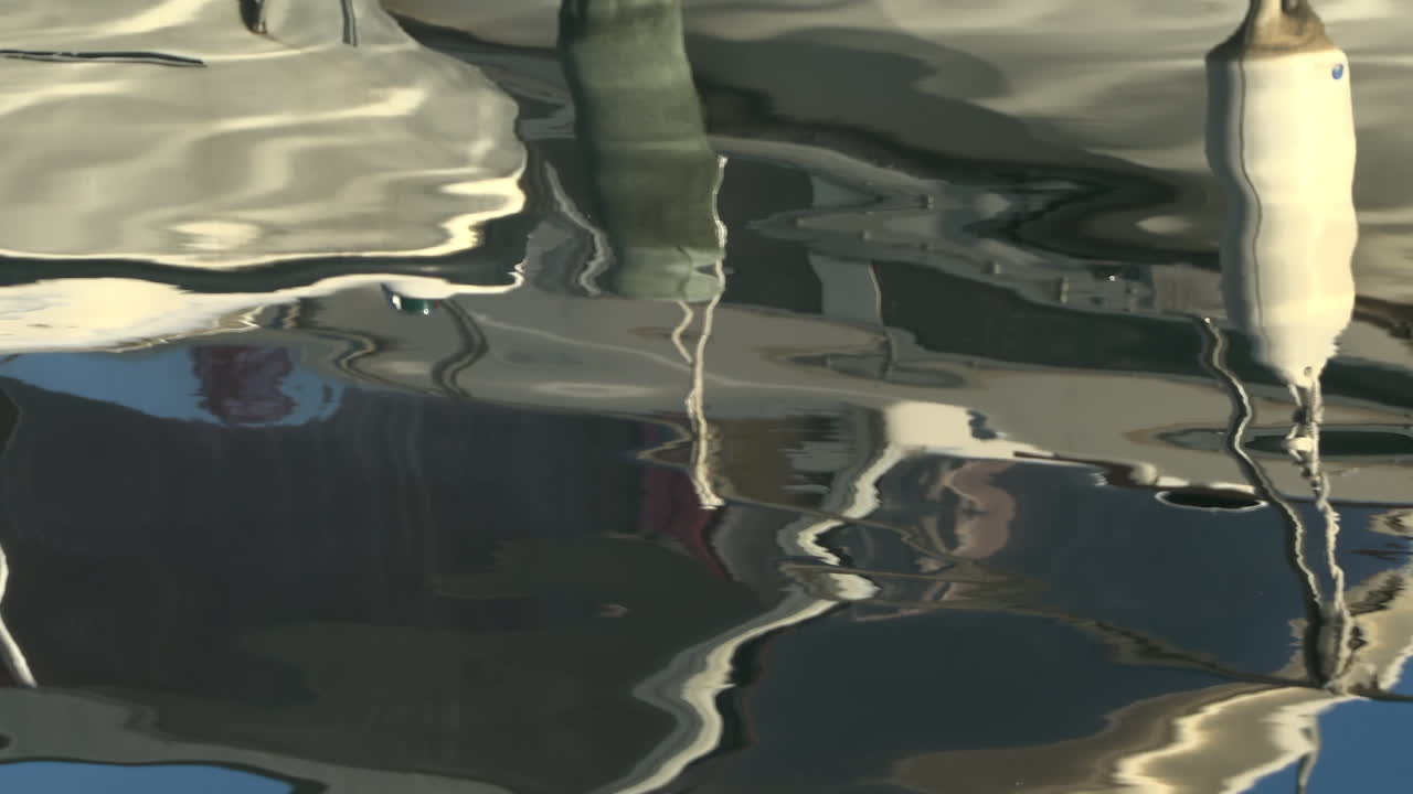 The reflection of the side of a boat docked in the water, with fenders hanging from its hull