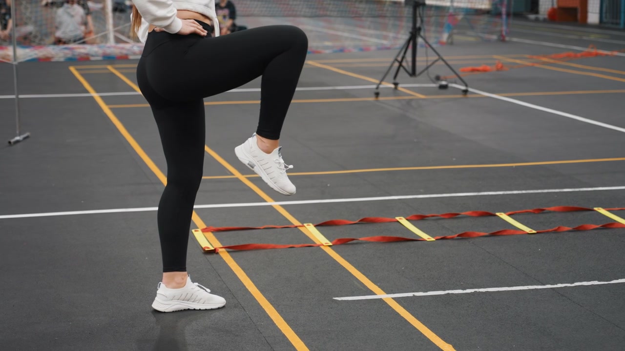 Badminton court ladder drill demo white female athlete showcasing polished footwork, confident singleleg lifts and measured pacing on indoor marked court with audience and camera setup, instructional