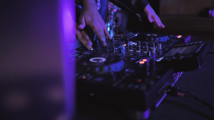 Mani di DJ che regolano un mixer musicale in un club buio con luci viola