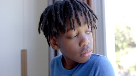 thoughtful african american boy looking through window at home, slow motion