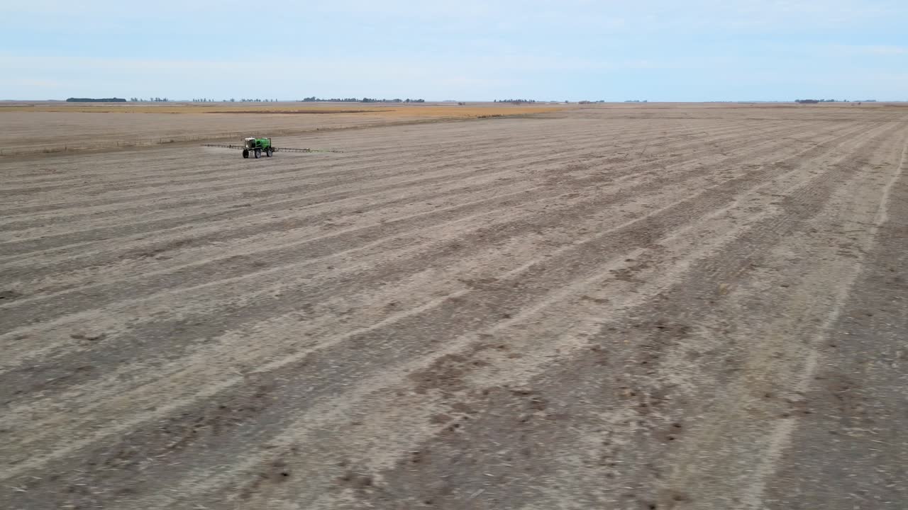 Aerial panoramic of a field in La Pampa, Argentina, a tractor actively spraying crops under an open sky