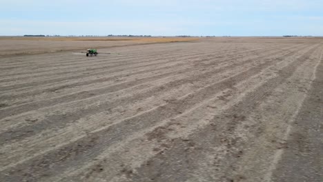 aerial panoramic of a field in la pampa, argentina, a tractor actively spraying crops under an open sky