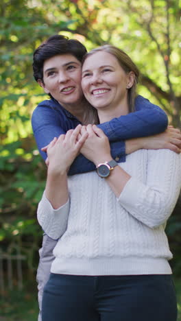 video vertical de una feliz pareja de lesbianas caucásicas abrazándose en el jardín