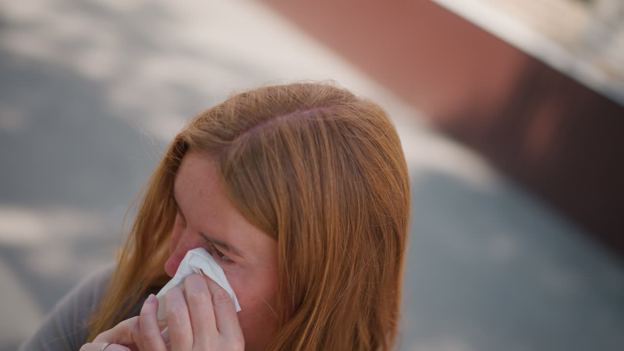 Top view of sad mum standing outdoors cleaning tears with wipes, emotional expression showing quiet grief and reflection, wind moving through hair, soft light capturing vulnerability