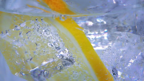 extreme close up of a tasty lemon slice in a jar of sparkling water with ice cubes slowly moving around