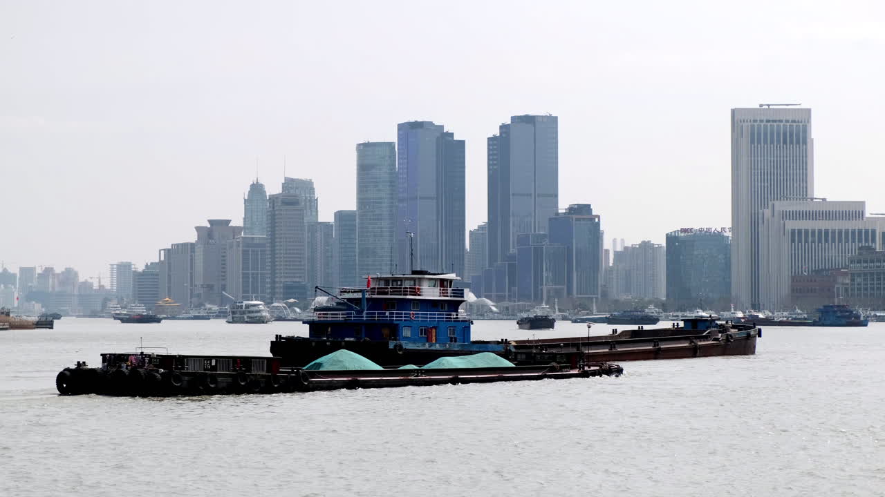 Cargo barges sail along the Huangpu River with Shanghai’s modern skyscrapers rising in the background