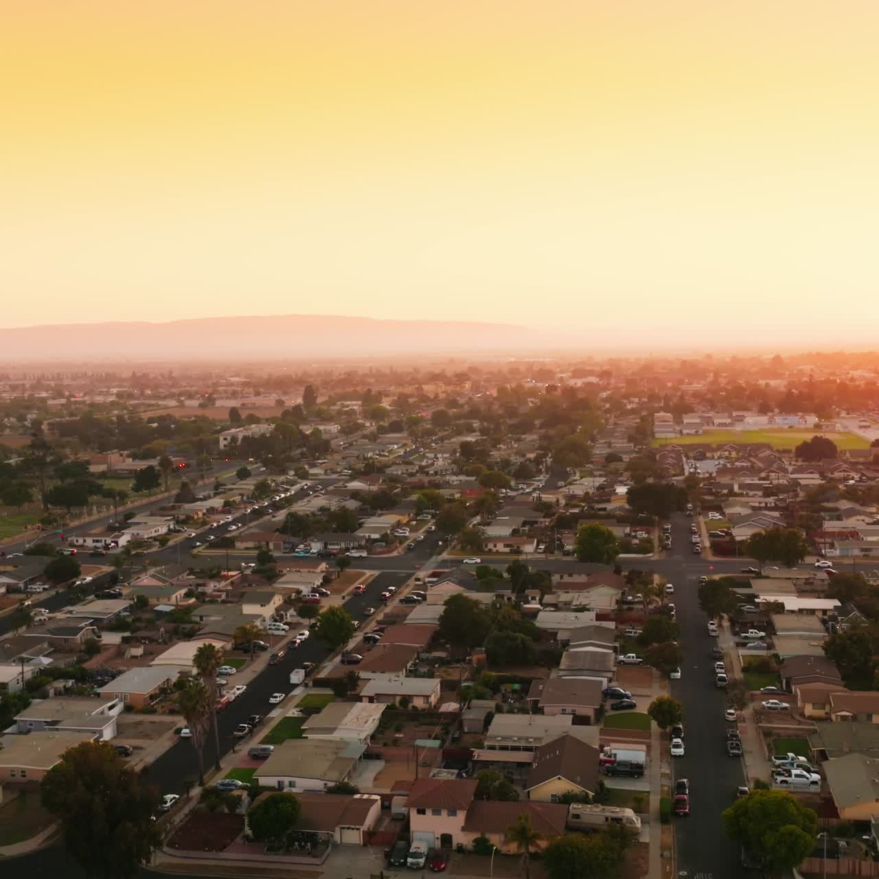 Lovely scenery of a usual city in United States. Straight quarters of residential area with plain streets and lots of cars at the roadside. Yellow sky at backdrop