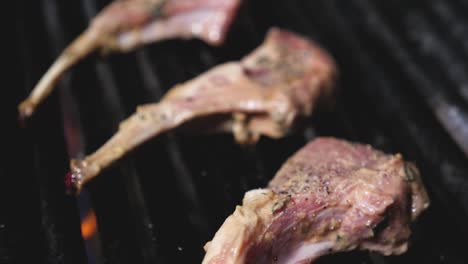 lamb chops roasting on bbq grill in professional kitchen flames kicking up smoking cooking the raw meat on black cast iron grill tight panning down