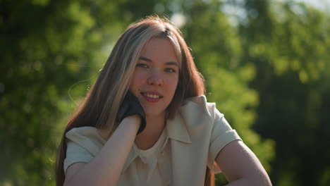 young lady leaning on bike with hand on chin handlebar with a gentle smile, looking contemplative under warm sunlight, blurred background of lush green foliage