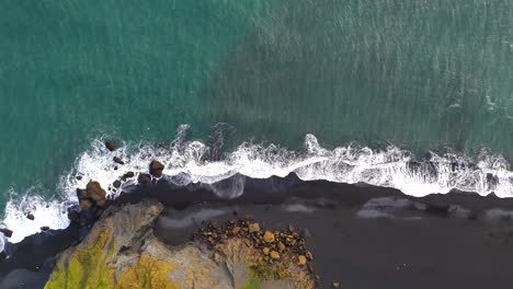 top down aerial view of the black sand beach in southern iceland, rocky coastline with waves splashing the black sand beach