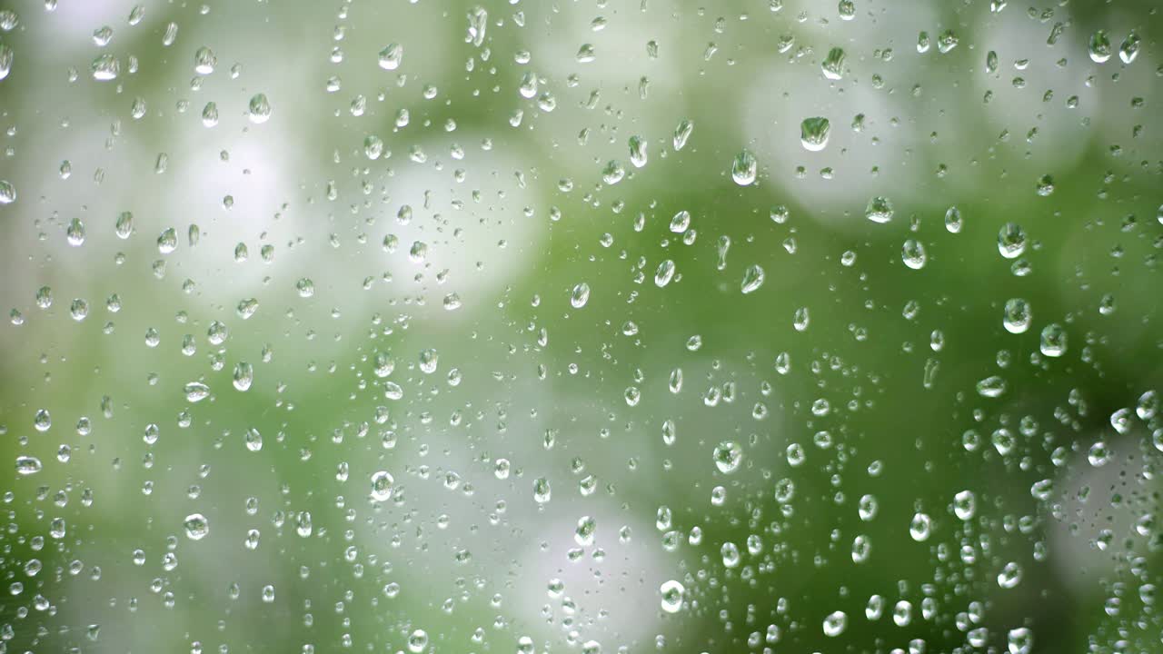 4k Close-up footage of raindrops splashing against a window glass with light leaks.