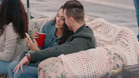 felices amigos multiétnicos disfrutando de una fiesta de fin de semana en la azotea una joven pareja usando un teléfono inteligente navegando por las redes sociales compartiendo una conexión romántica