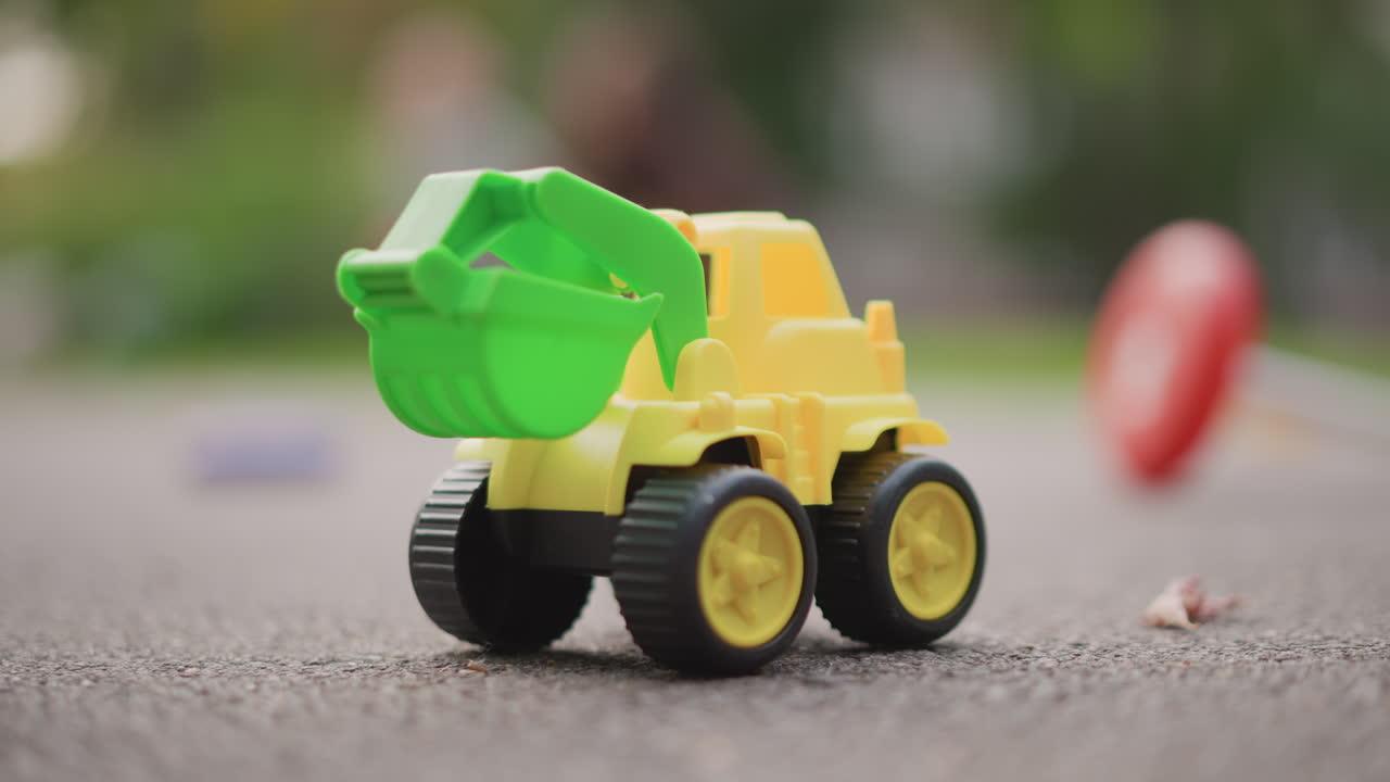 Caminhão de brinquedo verde e amarelo no pavimento, foco raso macro e bokeh suave. Caminhão basculante de plástico sobre asfalto texturizado após brincar ao ar livre, rodas em detalhes nítidos, fundo de parque desfocado, luz solar quente.