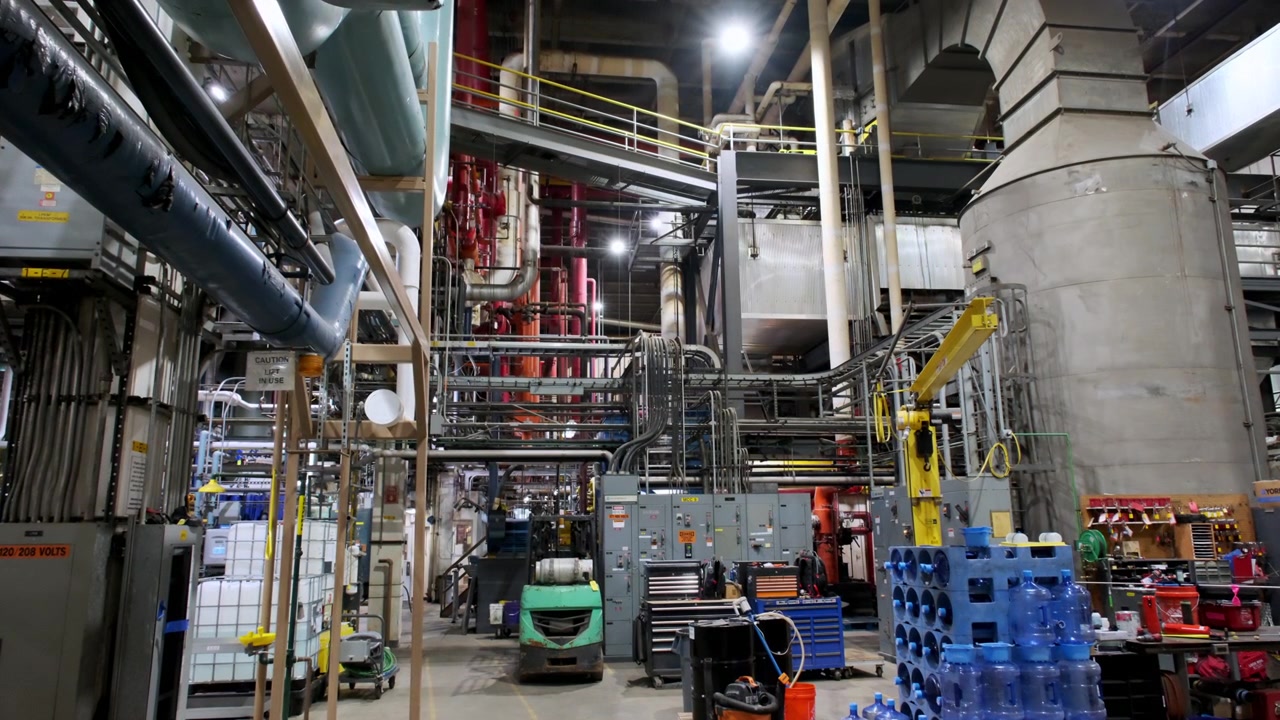 Industrial facility with interconnected machinery, storage tanks, pipelines, and a forklift.