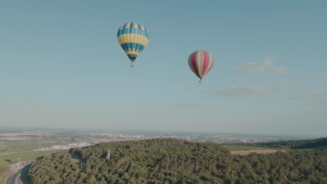 4k аэрофотосъемка двух воздушных шаров над лесом с городом на заднем плане