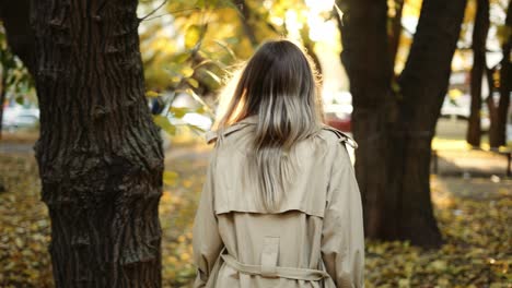 Rückansicht-Einer-Eleganten-Frau,-Die-Im-Trenchcoat-Durch-Den-Herbstpark-Spaziert