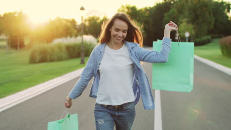 Happy-woman-holding-shopping-bag-walking-on-street-at-sunset