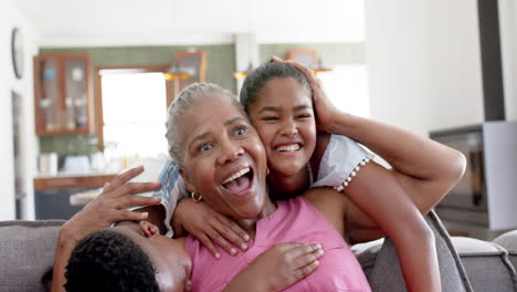 happy african american grandchildren embracing grandmother on sofa, slow motion