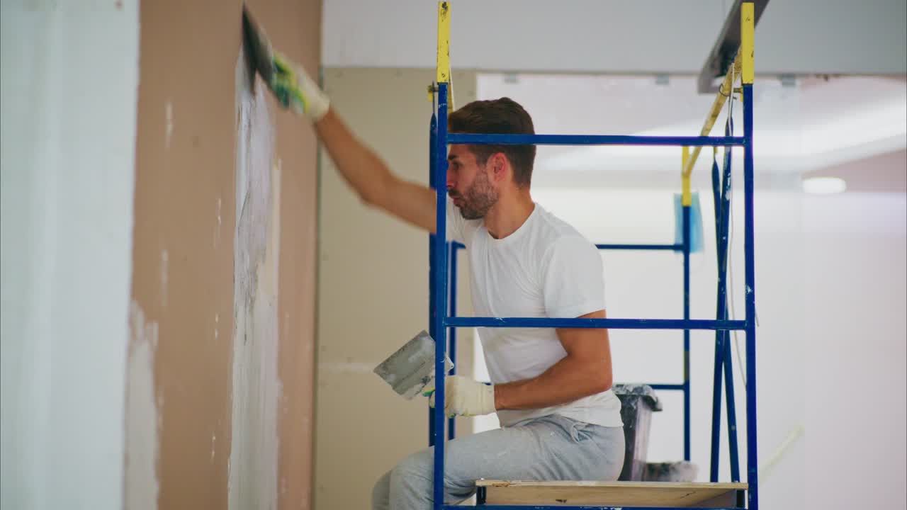 Skilled Man on Scaffold Applying Fresh Plaster to Drywall; Emphasizing the Art of Home Renovation and Meticulous Craftsmanship in Action