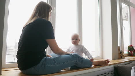 Mutter-Mit-Baby-Sitzt-Am-Fenster-Und-Spielt