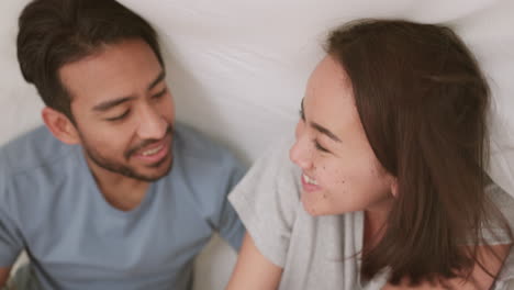 happy couple laughing under blanket in bed