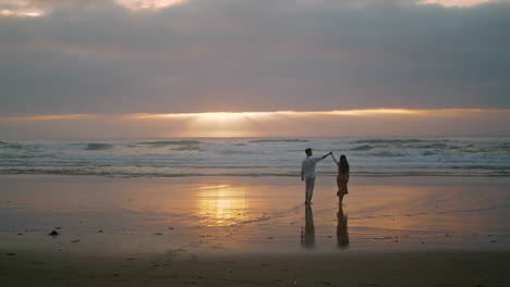 unos recién casados cariñosos van a la orilla del mar al amanecer. una pareja mirando el océano verticalmente.