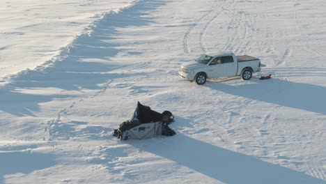 2-Women-setting-up-a-tent-shelter-on-the-snow,-frozen-lake,-drone