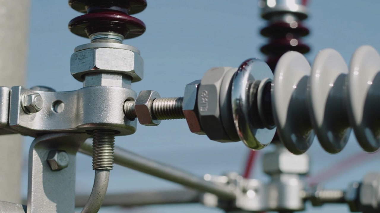 Panorerende kamera afslører en isolatorstreng på en elmast, der viser klemme, gevindstang og sekskantmøtrikker.
