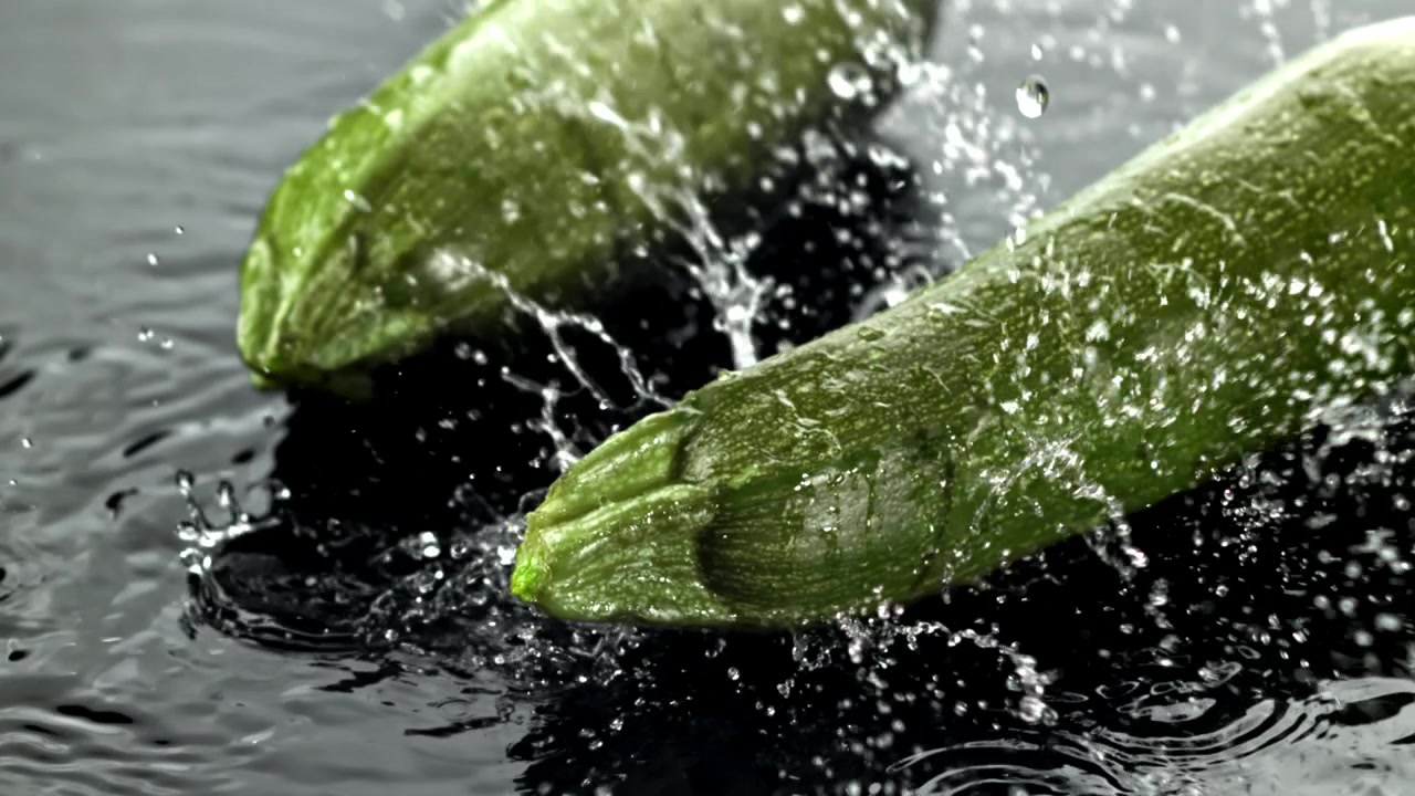 Acqua che schizza al rallentatore su zucchine verdi fresche.