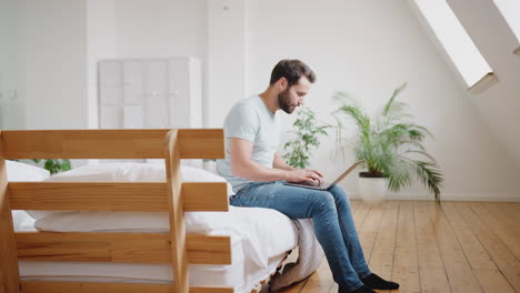 Un-Joven-Sentado-En-La-Cama-En-Un-Apartamento-Tipo-Loft-Trabajando-En-Una-Computadora-Portátil