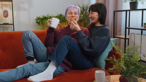 two lesbian women family couple girl friends drinking coffee eating croissants and talking at home