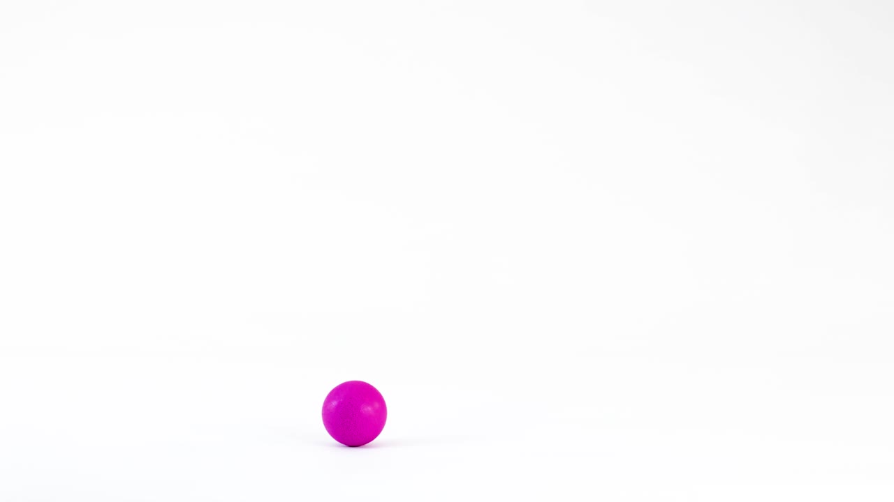 A bright purple sphere rolls smoothly across a clean white studio floor in slow motion