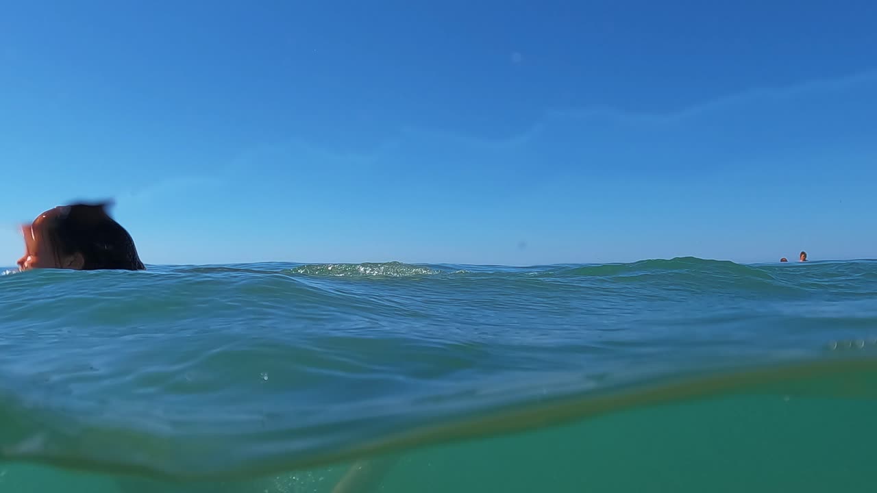 수평선을 배경으로 바닷물에서 공중제비를 하는 어린 빨간 머리 소녀의 반 수중 장면