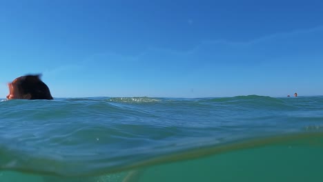 Half-underwater-scene-of-young-redhead-girl-somersaulting-back-flip-in-sea-water-with-horizon-in-background