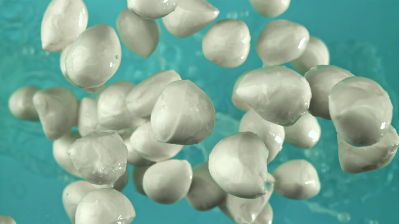 Super slow motion di palline di mozzarella che galleggiano in acqua blu