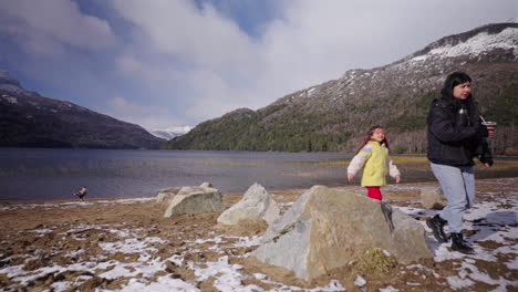 Family exploring lakeshore in snowy mountainous landscape while drinking mate, Lago Falkner, Argentina